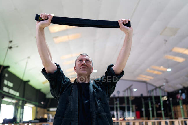 Basso angolo di grave uomo adulto in nero indossare esercizio con banda di resistenza durante l'allenamento kajukenbo nella moderna palestra di arti marziali — Foto stock