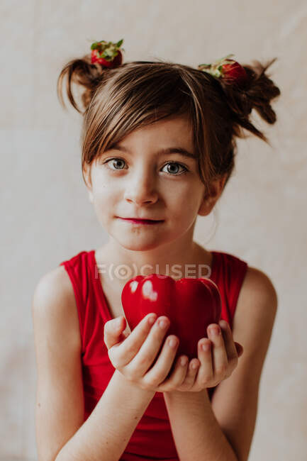 Чарівна маленька дівчинка з полуницею в волоссі показує свіжий перець і дивиться на камеру — стокове фото
