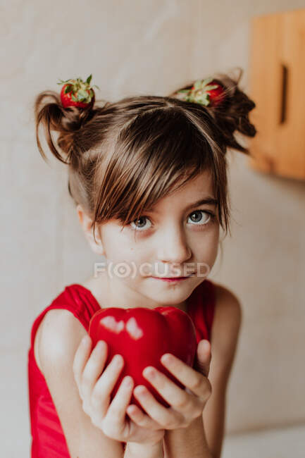 Adorabile bambina con fragole in capelli che mostrano pepe fresco e guardando la fotocamera — Foto stock