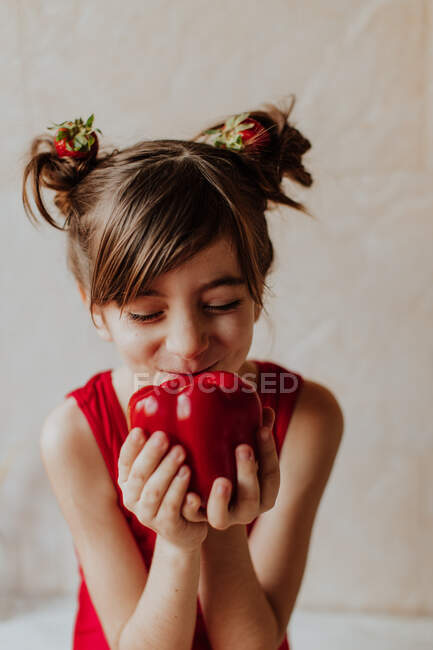 Adorable niña con fresas en el pelo mostrando pimienta fresca con los ojos cerrados - foto de stock