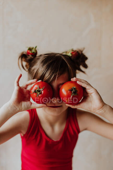 Menina bonito mantendo tomates frescos perto dos olhos, enquanto se divertindo na cozinha em casa — Fotografia de Stock