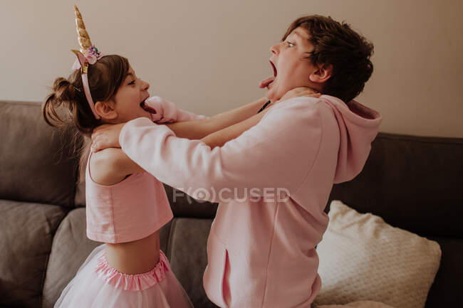 Vista lateral do irmão e da irmã em roupas rosa estrangular uns aos outros enquanto luta perto do sofá em casa — Fotografia de Stock