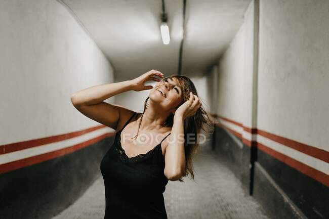 Giovane femmina in elegante abito nero in piedi in un passaggio sotterraneo chiuso e guardando in alto sognante — Foto stock