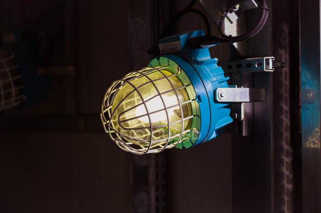 Relâmpago industrial antigo com lâmpada luminosa protegida por caixa de grade de metal e colocado no porão da planta — Fotografia de Stock