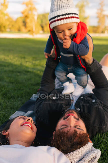 Пара лежить на ковдрі на зеленій траві і тримає милого малюка в теплому одязі, відпочиваючи під час вихідних у парку — стокове фото