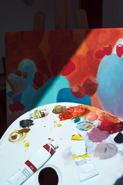 Chaotische Palette mit Pigmentflecken und Tuben in der Nähe der Staffelei mit abstrakter Malerei — Stockfoto