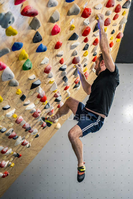 From bellow strong male athlete in sportswear climbing on colorful wall during workout in modern climbing center — Stock Photo