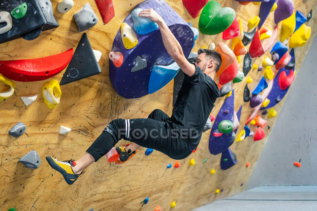 From bellow side view of strong male athlete in sportswear climbing on colorful wall during workout — Stock Photo