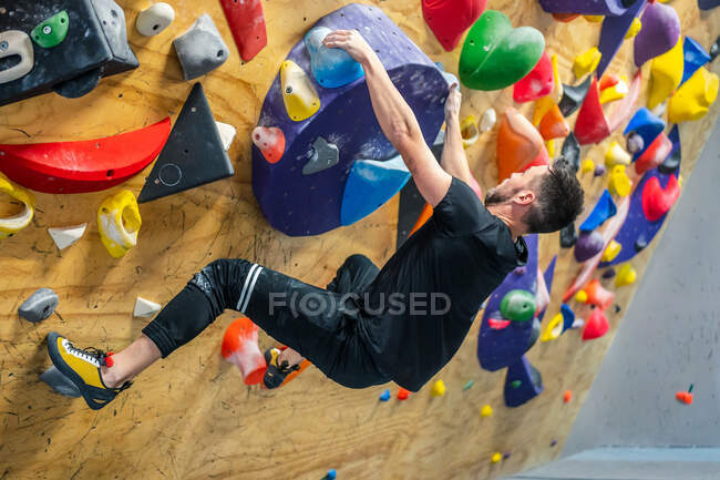 From bellow of unrecognizable strong male athlete in sportswear climbing on colorful wall during workout in modern guy — Stock Photo