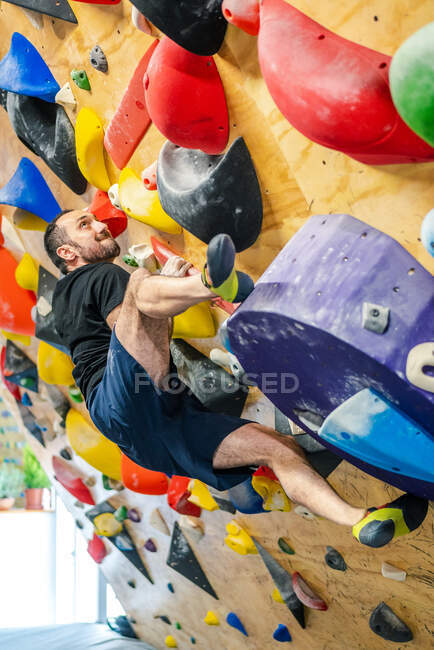 From bellow strong male athlete in sportswear climbing on colorful wall during workout in modern guy — Stock Photo