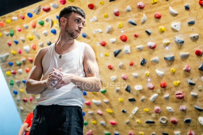 D'en bas de jeune homme en tenue de sport debout et regardant loin avec mur d'escalade sur fond flou — Photo de stock