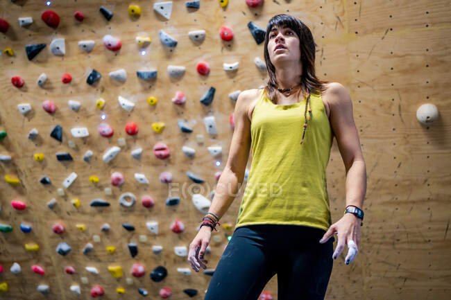 From below of young female athlete in sportswear standing near climbing wall in gym — Stock Photo