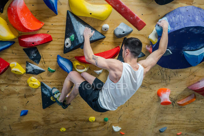 З дзвону невпізнаваний сильний чоловік спортсмен в спортивному одязі, сходження на барвисту стіну під час тренування в сучасному хлопці — стокове фото