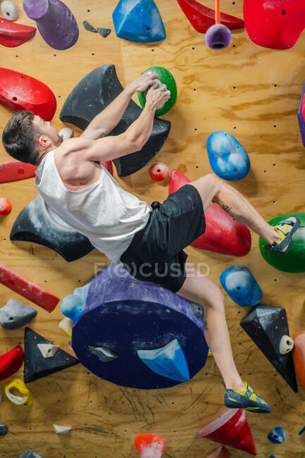 Dal soffietto irriconoscibile forte atleta maschile in abbigliamento sportivo arrampicata su parete colorata durante l'allenamento nel moderno centro di arrampicata — Foto stock
