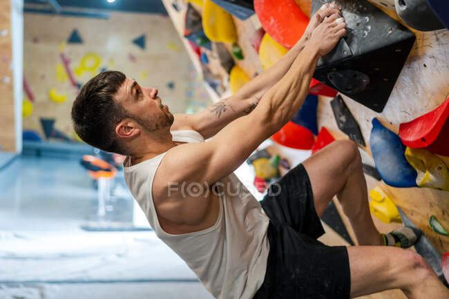 Vista lateral do atleta masculino forte no sportswear escalando na parede colorida durante o treino no cara moderno — Fotografia de Stock