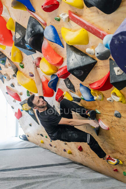 From bellow strong male athlete in sportswear climbing on colorful wall during workout in modern guy — Stock Photo