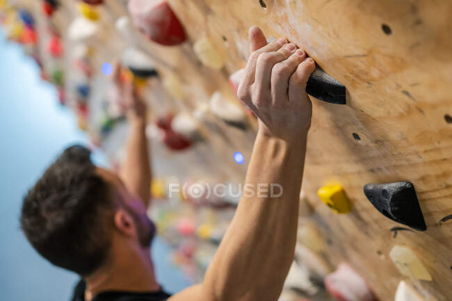 Vista lateral do atleta masculino forte anônimo borrado em sportswear escalando na parede colorida durante o treino no cara moderno — Fotografia de Stock