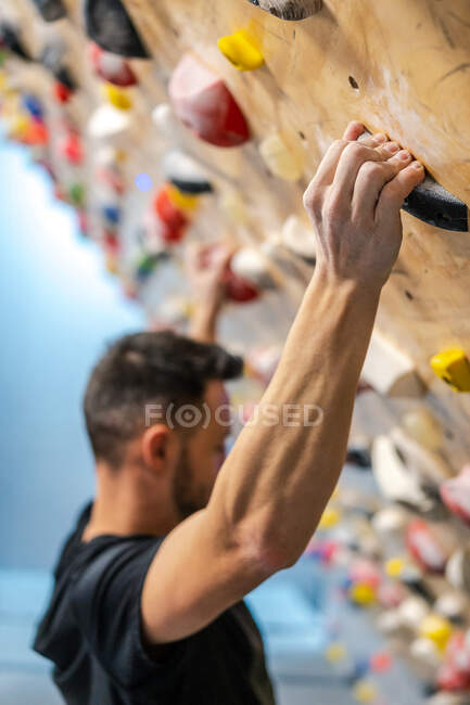 Vista lateral do atleta masculino forte anônimo borrado em sportswear escalando na parede colorida durante o treino no cara moderno — Fotografia de Stock