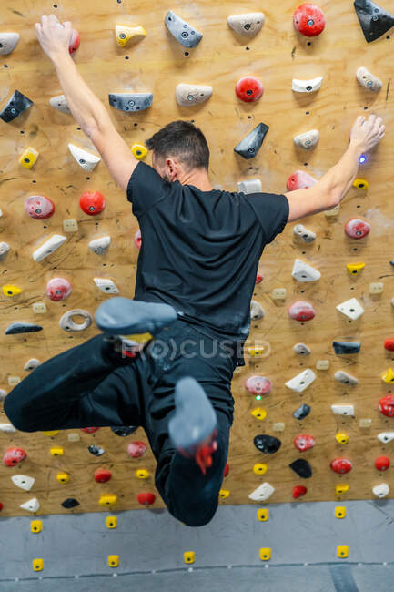 Vista posteriore del giovane in tenuta attiva afferra saldamente mentre appeso in aria durante l'allenamento di arrampicata in palestra — Foto stock