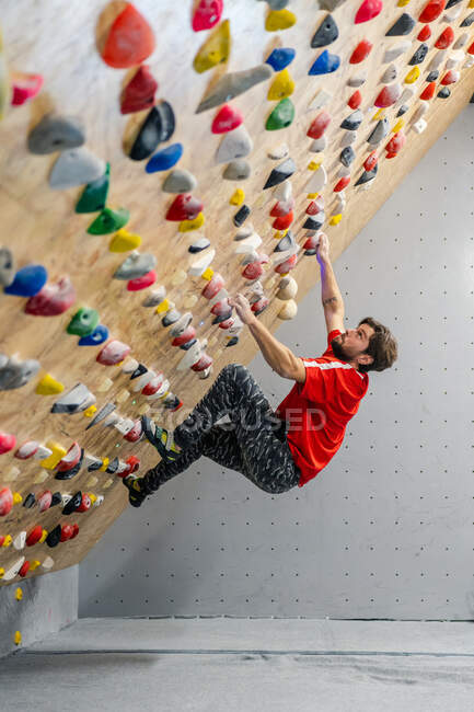 Aus der Seitenansicht eines starken männlichen Athleten in Sportbekleidung, der während des Trainings in einem modernen Kerl an einer bunten Wand klettert — Stockfoto