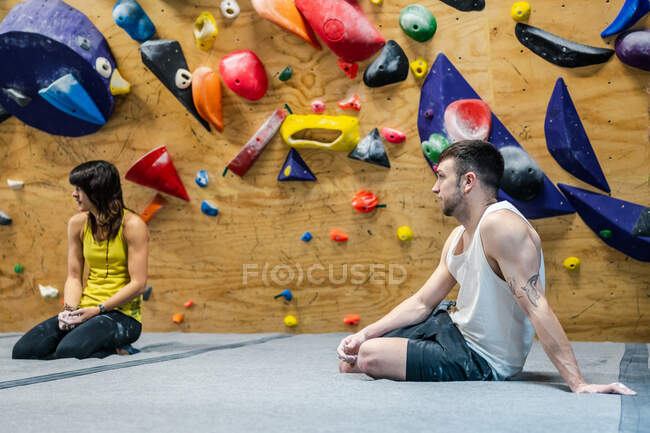 Vista laterale di muscoloso uomo e donna sorridenti seduti sul pavimento e sorridenti mentre si allenano in palestra di arrampicata — Foto stock