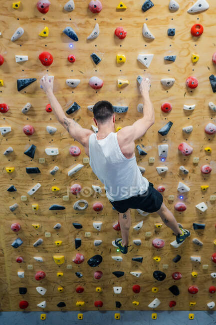 From bellow unrecognizable strong male athlete in sportswear climbing on colorful wall during workout in modern guy — Stock Photo