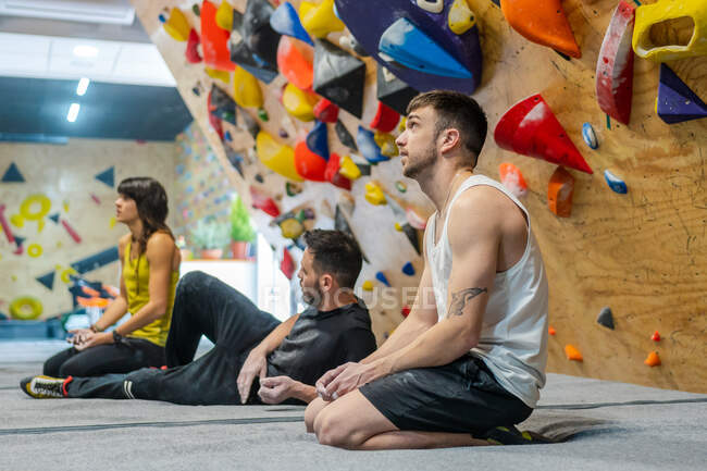 Side view of muscular smiling men and woman sitting on floor and smiling away while having training in climbing gym — Stock Photo