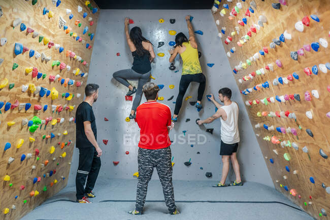 Back view of young group of strong male and female climbers having training on wall in modern gym — Stock Photo