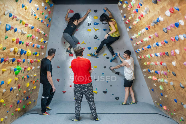 Back view of young group of strong male and female climbers having training on wall in modern gym — Stock Photo