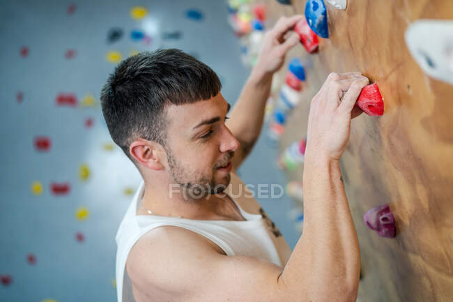 Vista lateral de atleta masculino fuerte en la escalada de ropa deportiva en la pared colorida durante el entrenamiento en chico moderno - foto de stock