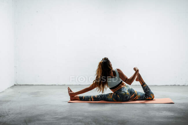 Вид збоку молодої гнучкої жінки в спортивному одязі роблять спереду розділений з піднятою ногою, сидячи на підлозі — стокове фото
