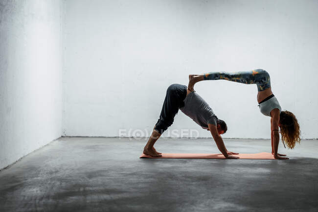 Side view of adult man in Downward Facing Dog pose and woman in handstand leaning on back of partner — Stock Photo