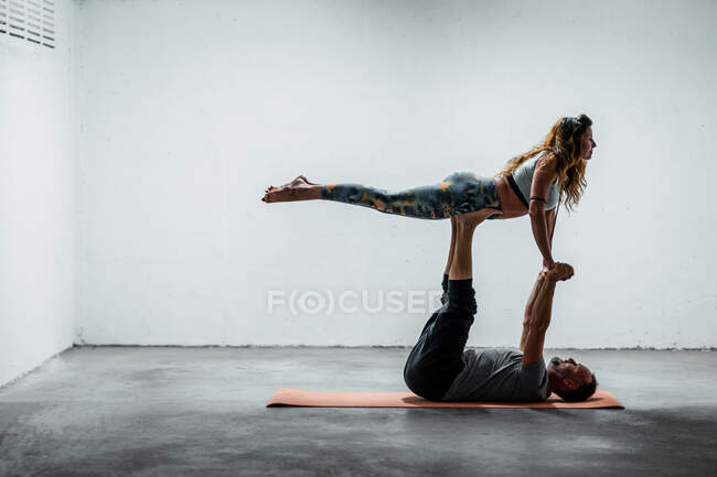Vue latérale d'un couple adulte faisant du yoga par paire à Front Bird posant sur un tapis et se tenant la main — Photo de stock