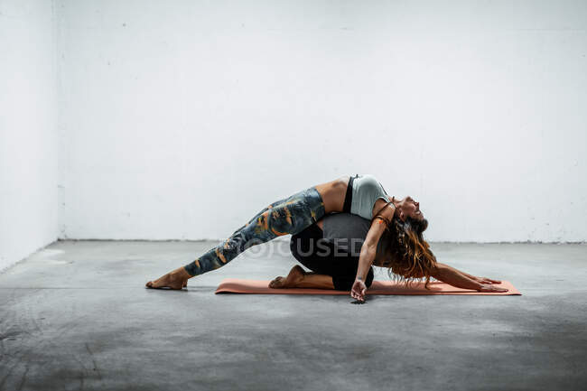 Side view of flexible man in Child pose and slim woman in Fish pose on back of partner lying on mat — Stock Photo
