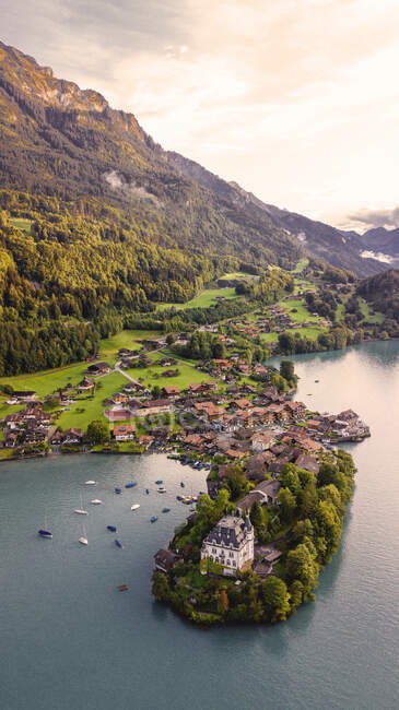 Von oben Drohnenblick auf kleine Halbinsel mit altem Schloss Iseltwald und Dorf am Ufer des Sees in bergigem Gelände in der Schweiz bei Sonnenuntergang am Sommerabend — Stockfoto