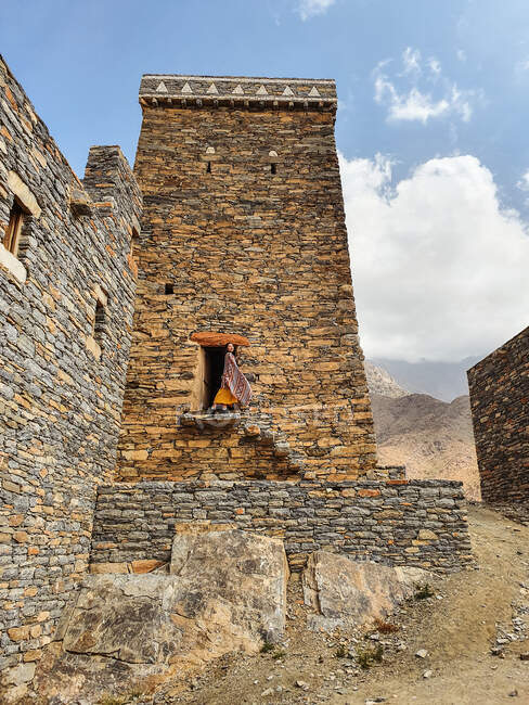 From below of monumental ancient building with remote female tourist coming out of doorway in yellow dress while enjoying hot sunny day in Marble Village in Al Bahah — Stock Photo