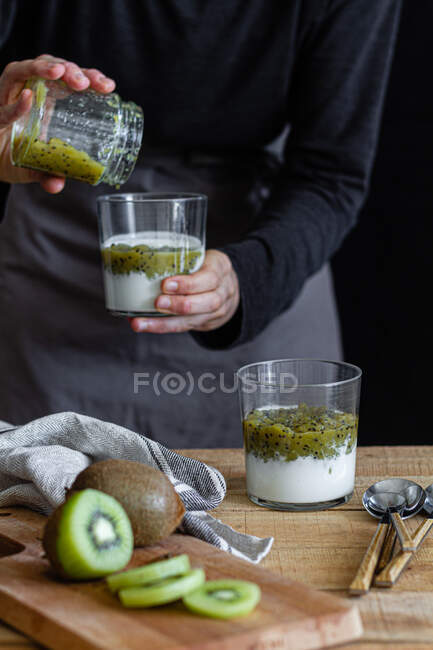 Cropped shot of woman in apron preparing yogurt with fresh mashed kiwi — Stock Photo