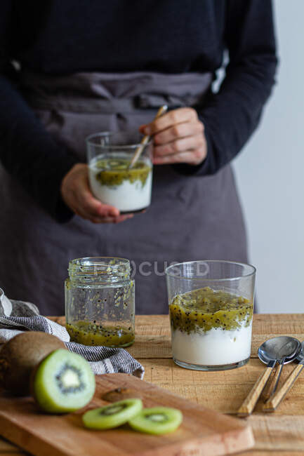 Tiro cortado de mulher em avental preparando iogurte com purê de kiwi fresco — Fotografia de Stock