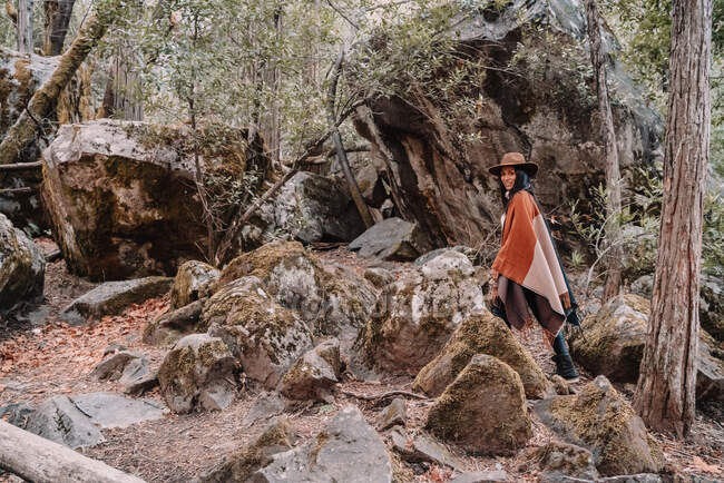 Jeune randonneuse en boho élégant et chapeau debout parmi les rochers géants dans la forêt pendant le voyage au parc national de Yosemite en Californie — Photo de stock