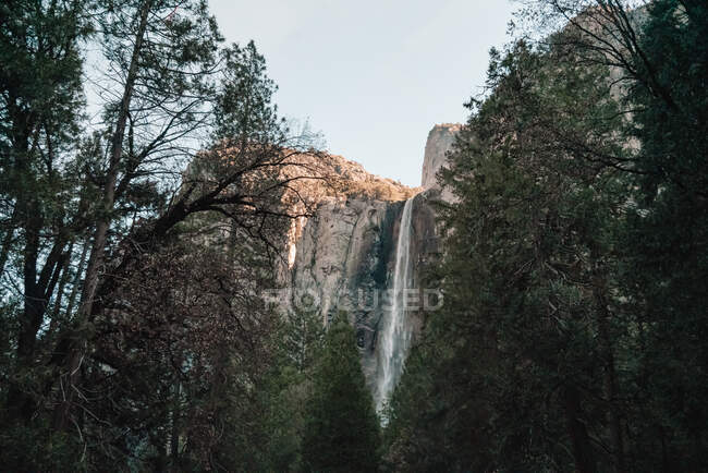A partir de baixo vista incrível de poderosa cachoeira fluindo de alta penhasco rochoso contra céu sem nuvens em dia ensolarado no Parque Nacional de Yosemite, nos EUA — Fotografia de Stock