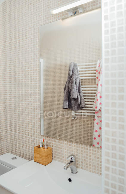 Weiche Bademäntel spiegeln sich im Spiegel des modernen Badezimmers mit Keramikwaschbecken und Fliesen wider — Stockfoto