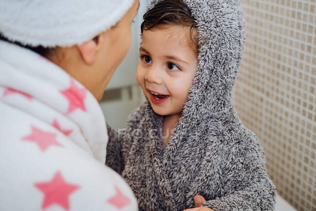 Cortado mujer irreconocible con un niño pequeño en albornoz después de tomar la ducha y mirarse entre sí - foto de stock