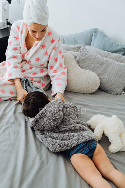 Von oben zufriedene Frau im Bademantel, die Spaß mit kleinem Jungen auf weichem Bett hat und sich gegenseitig ansieht — Stockfoto