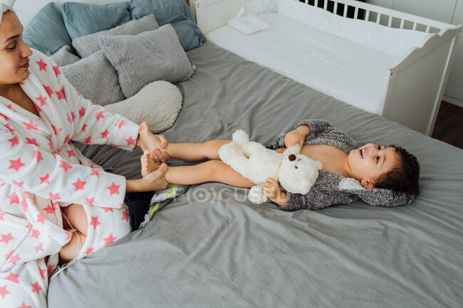 De cima de mulher conteúdo em roupão de banho se divertindo com o menino na cama macia — Fotografia de Stock
