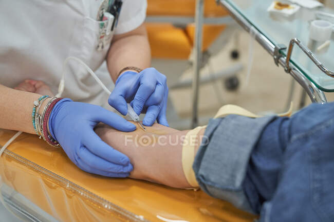 Женщина-специалист в латексных перчатках, выполняющая инъекцию шприца анонимному пациенту во время процедуры переливания крови в больнице — стоковое фото