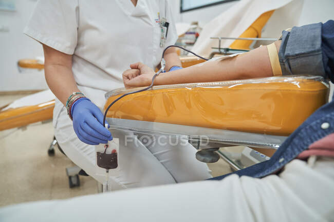 Crop female medical specialist in latex gloves performing injection with syringe to anonymous patient during procedure of blood transfusion in hospital — Stock Photo