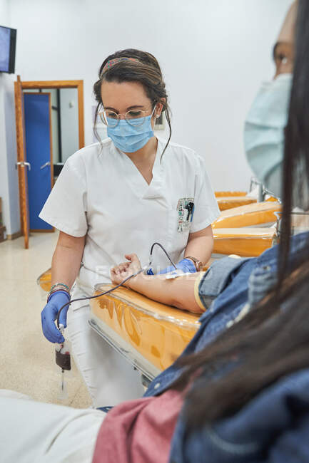 Mujer especialista en guantes de látex que realiza la inyección con jeringa al paciente anónimo durante el procedimiento de transfusión de sangre en el hospital — Stock Photo