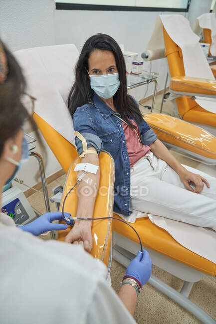 Женщина-специалист в латексных перчатках, выполняющая инъекцию шприца анонимному пациенту во время процедуры переливания крови в больнице — стоковое фото