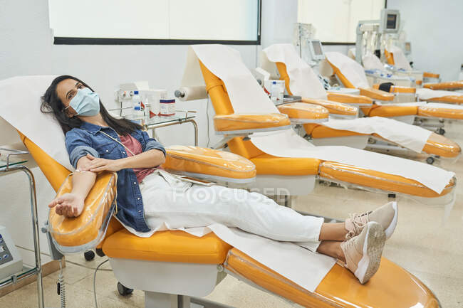 Female donor with patch on hand sitting in medical chair after blood transfusion procedure — Stock Photo