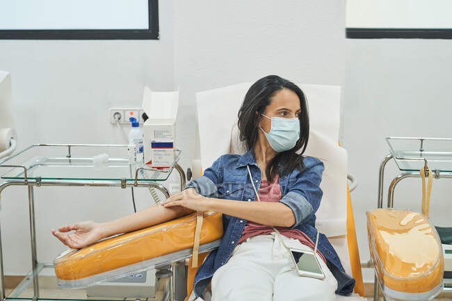 Female donor with patch on hand sitting in medical chair after blood transfusion procedure — Stock Photo